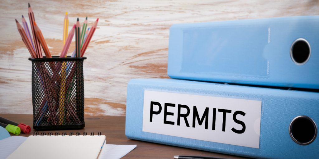 Blue office binders labeled "PERMITS" with pencil holder on wooden desk representing documentation needed for shipping wine across country permit and restrictions compliance.