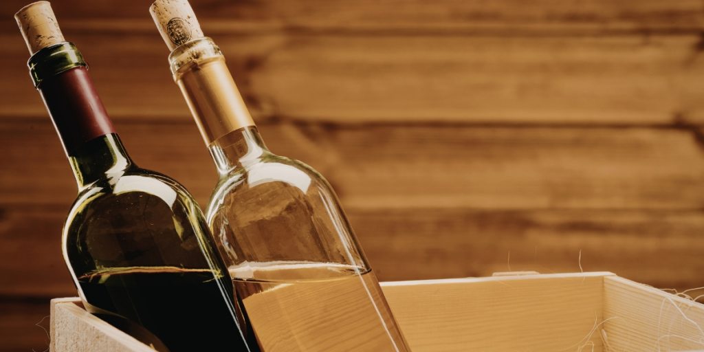 Common wine shipping mistakes illustrated with red and white wine bottles displayed in a wooden crate against a rustic wooden background.