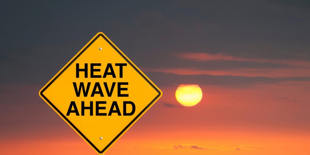 Shipping During Extreme Weather represented by a yellow warning sign against a dramatic sunset sky with intense heat and glowing sun.