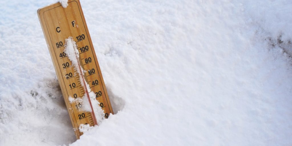 A wooden thermometer partially buried in snow shows freezing temperature conditions during winter weather.