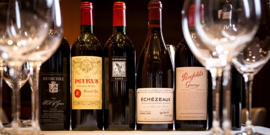 Collection of premium vintage wine bottles including Petrus, Screaming Eagle, and Echezeaux displayed with wine glasses for shipping rare wines