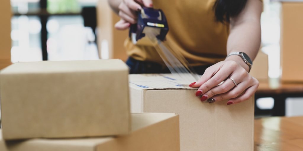 Choose the Right Wine Shipping Coverage as person in mustard sweater carefully seals cardboard box with packing tape for shipment