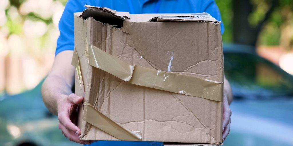 Evidence You Need for Wine Damage Claims shown by delivery person in blue shirt holding severely crushed damaged cardboard package