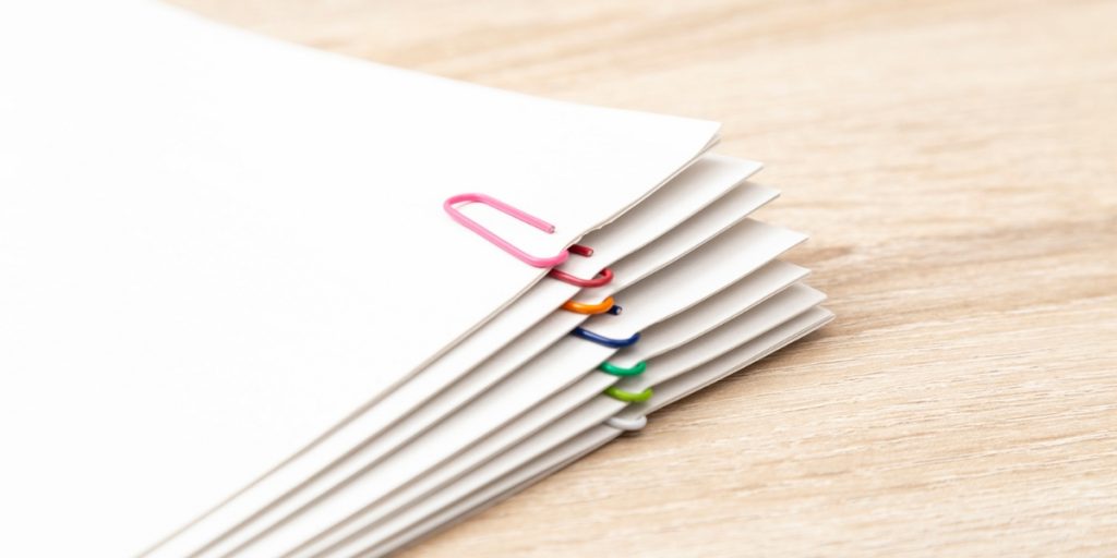Supporting Documentation organized with colorful paper clips securing white papers on light wooden desk surface