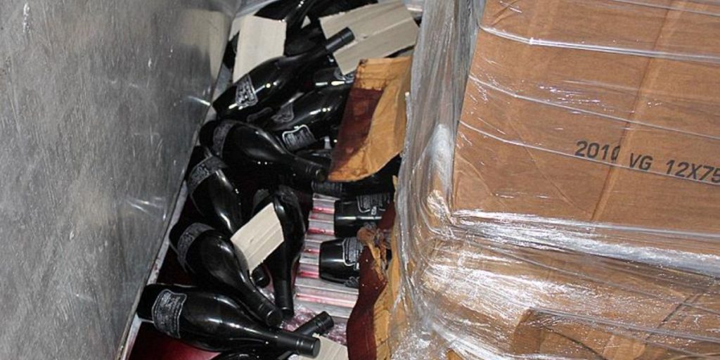 Wine shipment damage claims showing broken wine bottles with red wine stains next to wrapped cardboard boxes