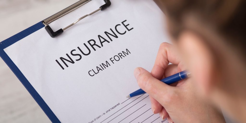 Wine shipping insurance coverage claim form on clipboard as hand with blue pen completes insurance documentation