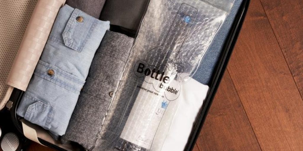 Suitcase packed with wine bottle protection wrap and protective bubble packaging showing flying with wine vs shipping wine comparison with travel gear and protective materials for wine transport