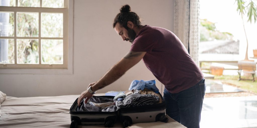 Man packing wine bottles in suitcase with protective wrapping and clothing demonstrating how to pack wine in a suitcase safely for air travel with proper cushioning and protection
