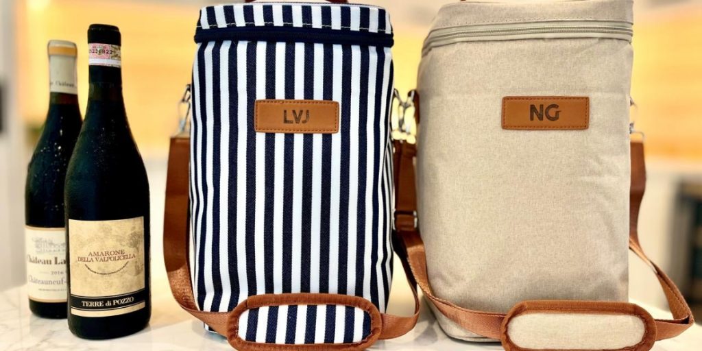 Two stylish wine travel bags with leather handles and personalized initials displayed next to premium wine bottles, showcasing fashionable wine travel bags designed for convenient wine transport and storage.