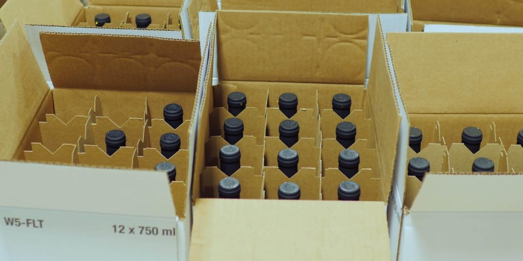Wine club shipping - cardboard shipping boxes with wine bottles packed in protective dividers ready for shipment, displaying wine bottles with black caps and secure packaging materials for safe wine club delivery
