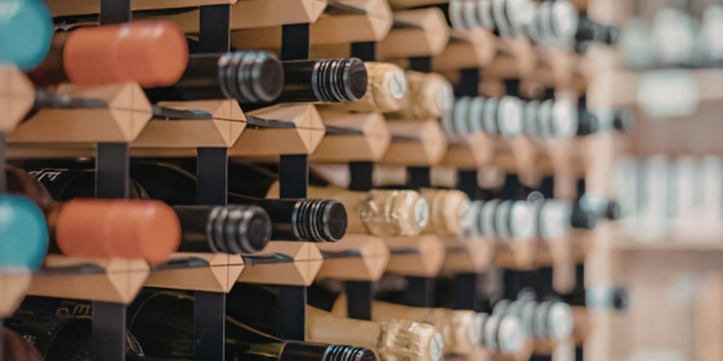 Wine club logistics depicting multiple wine bottles with various colored capsules and labels organized systematically on wooden wine racks in a professional storage environment.
