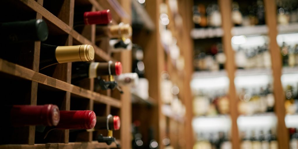 Wine club logistics showing carefully arranged wine bottles with red and gold labels displayed on wooden shelves in a temperature-controlled wine storage facility.