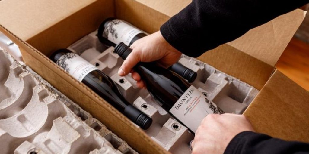 Wine shipping compliance – person packing wine bottles in protective cardboard box with foam inserts and proper protective cushioning for safe compliant wine shipment delivery