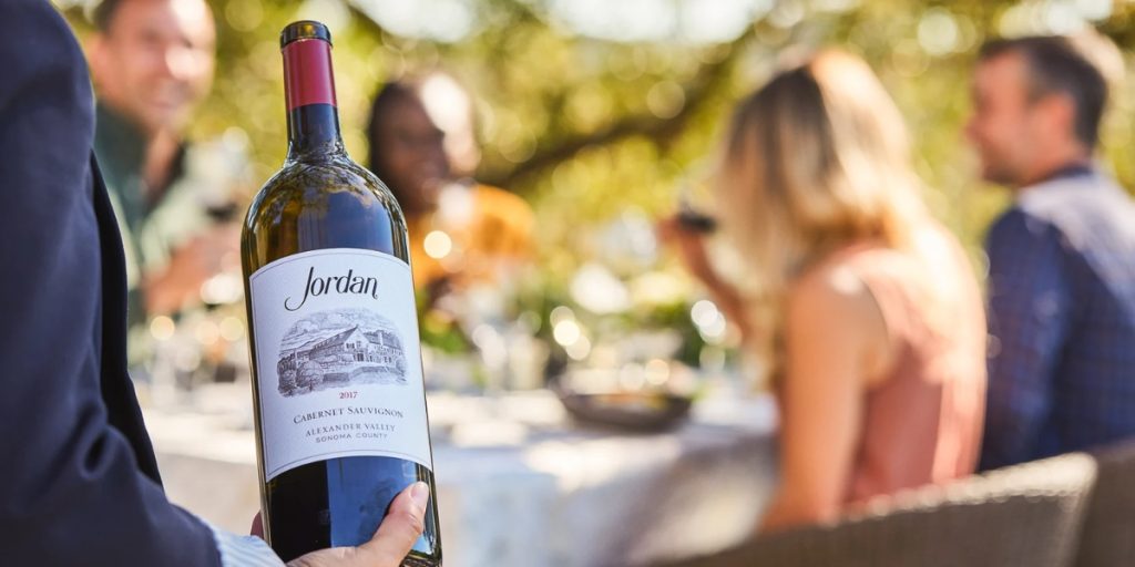 A server presents a bottle of Jordan Cabernet Sauvignon to guests dining outdoors, part of a selection that includes large format wine bottles.