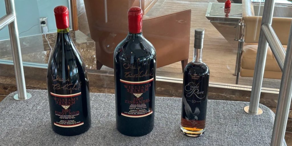 Two signed magnum bottles of Williams Selyem wine stand beside a whiskey bottle, showcasing large format wine bottles on display.